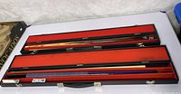 Two pool cues in open cases showing full length