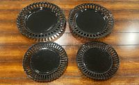 Four glossy black reticulated porcelain plates arranged on wood surface