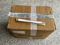 Sealed cardboard box with one wrapped white plastic knife on top