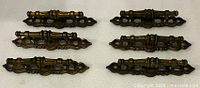 Front view of six matching brass drawer pulls showing ornate design