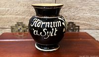 Front view showing cream script "Hörnum a. Sylt" on black glazed jar