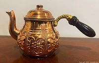 Right side view of engraved copper teapot showing spout, body design, lid and wooden handle
