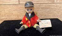 Front view of doll sitting, showing jacket and tag