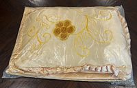 Bedspread and pillow folded in plastic showing embroidery and ruffled edge