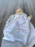 Full view of antique baby doll in white gown and knit cap
