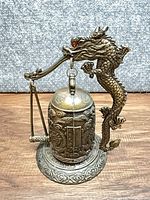 Full view of brass dragon stand holding cylindrical bell on patterned base