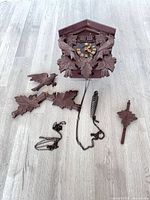 Full view of cuckoo clock body with detached leaf ornaments, one pinecone weight, chains and pendulum