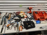 Overall view of table with toolbox, cordless drill, packaged gloves, rope, assorted hand tools