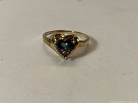 Front view of gold ring with heart-shaped mystic topaz on flat surface