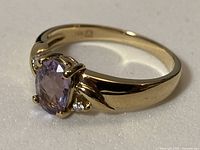 side view of gold ring with purple center stone and white accents