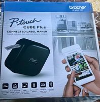 Retail box front showing Brother P-touch Cube Plus label maker and smartphone connectivity icons
