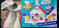 Front view of factory-sealed Snoopy & Friends Sno-Cone Machine box with two packs of paper cups