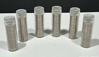 Six clear tubes standing upright filled with coins