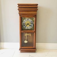 Front view of closed clock showing full case, dial, glass, pendulum