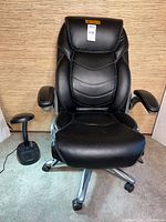Front view of black Wellness by Design office chair with adjustable armrests and desk lamp at side