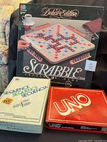 Three board game boxes: Deluxe Scrabble, Sequence, Deluxe Uno