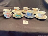 Overview of six teacups with saucers displayed on dark backdrop