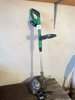 Full view of green cordless grass trimmer standing upright with battery and charger visible