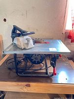 Table saw on wooden bench, side view showing frame, motor housing, blade and switch
