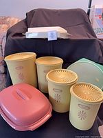 All six Tupperware pieces grouped: four yellow Servalier canisters, pink deviled-egg carrier, cream/brown steamer