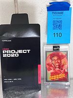 Front view of Bob Gibson Project 2020 card in protective case next to original black Project 2020 box