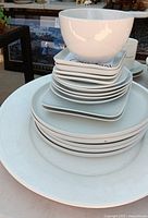 Stacked white Crate & Barrel dishes including bowl, square plates, round plates, large platter