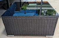 Full view of table showing woven rattan base and reflective glass top
