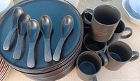 Stack of dinner plates, five soup spoons, six mugs visible