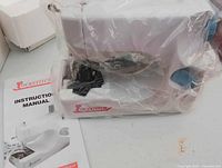 Lockstitch sewing machine wrapped in plastic beside instruction manual