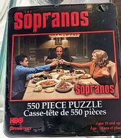 Front of sealed puzzle tin showing logo and dinner scene