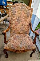 Front view of high-back upholstered armchair showing patterned fabric and carved wood arms and legs