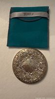 Front view of ornate sterling silver purse mirror and teal Towle pouch