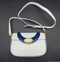 Full view of white and navy leather shoulder bag with strap displayed