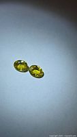 Two yellow-green oval sphene gemstones on neutral background