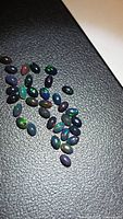 Group of small oval black opal cabochons on textured black background