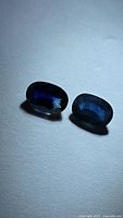 Two oval cut blue sapphires on white background