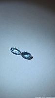 Two oval faceted pale-blue aquamarine gemstones on neutral background