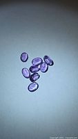 Eight oval purple amethyst gemstones on light background