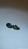 Two oval faceted blue-green sapphires on neutral background