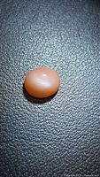 Peach-colored oval cabochon gemstone on textured dark surface