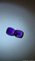 Pair of deep purple sugarloaf amethyst gemstones under light