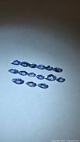 Fourteen pear and marquise tanzanites arranged in rows on neutral background