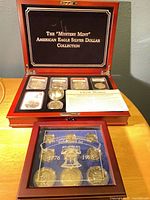 Display of both coin sets: Mystery Mint American Eagle Silver Dollar Collection case open showing five encapsulated coins and paperwork; Bicentennial Mint Mark Set closed case in foreground