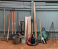 All items lined against fence showing long-handle tools, stakes, accessories