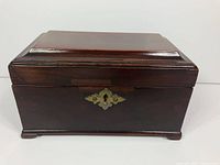 Front view of closed wooden tea caddy showing brass escutcheon and bracket feet