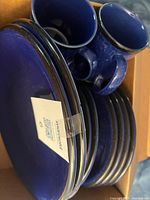 Stacked cobalt blue glass plates, bowls and mugs in box