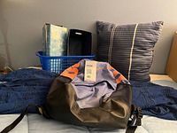 Backpack, cushion, plastic basket, magazine holder and cardboard storage box on bed