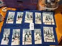 All ten quilted wall hangings laid out on table showing unique winter scenes