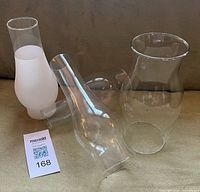 Group of four glass hurricane lamp chimney shades showing shapes and sizes
