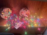 Two holly-pattern tins and lit multi-color string lights displayed